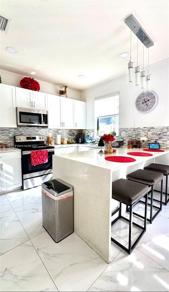 kitchen featuring a kitchen breakfast bar, white cabinetry, decorative light fixtures, and appliances with stainless steel finishes