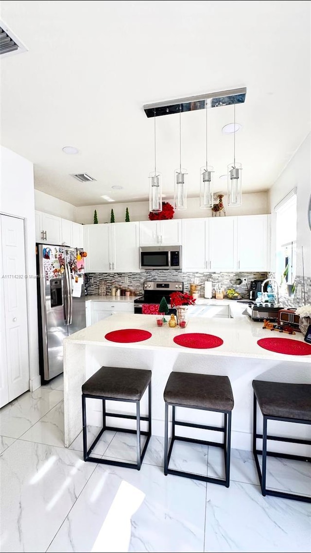 kitchen featuring a breakfast bar, hanging light fixtures, tasteful backsplash, white cabinetry, and stainless steel appliances