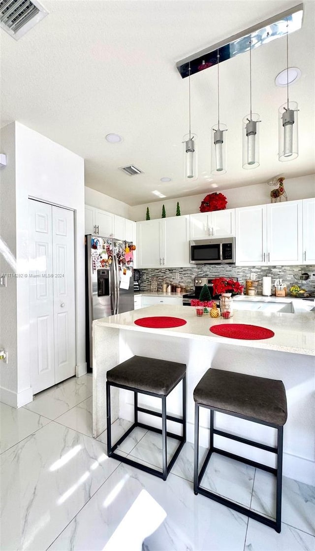 kitchen with stainless steel appliances, white cabinetry, hanging light fixtures, and a kitchen breakfast bar