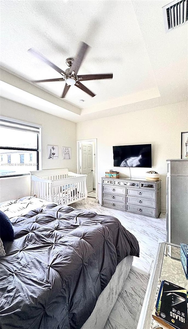 bedroom with a raised ceiling, ceiling fan, and a textured ceiling