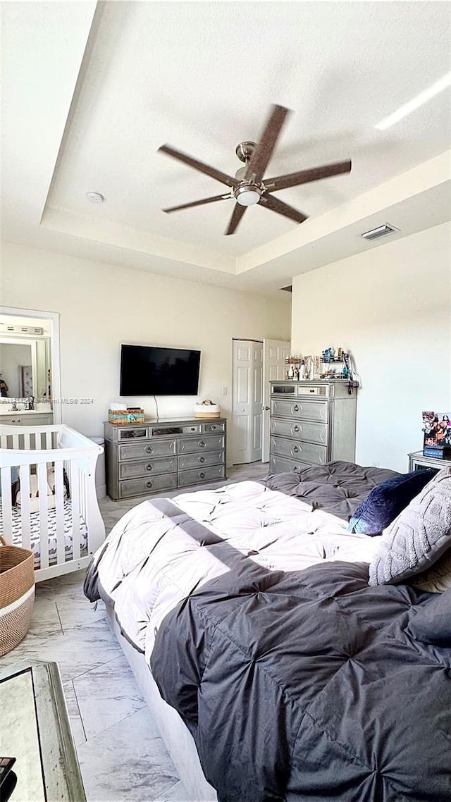 bedroom with a raised ceiling, ceiling fan, and a textured ceiling