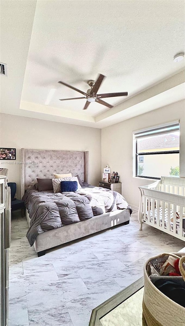 bedroom featuring a textured ceiling, a raised ceiling, and ceiling fan