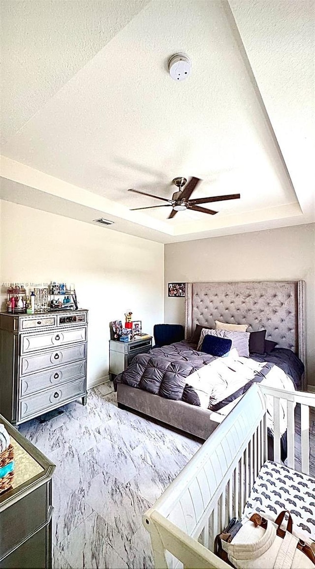 bedroom with ceiling fan, a textured ceiling, and a tray ceiling