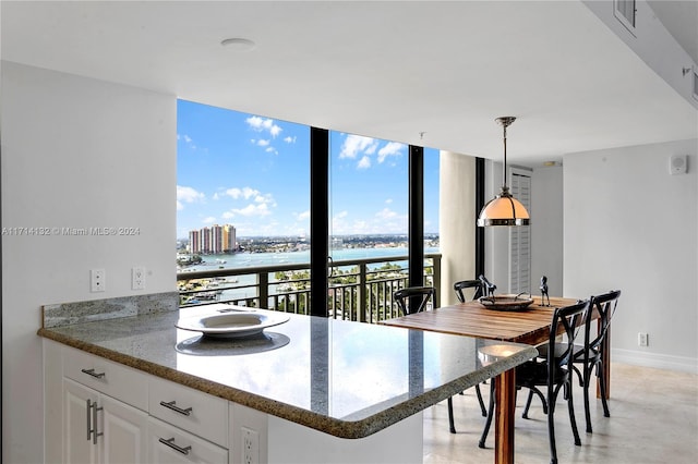 kitchen with white cabinetry, hanging light fixtures, a wall of windows, dark stone countertops, and a water view