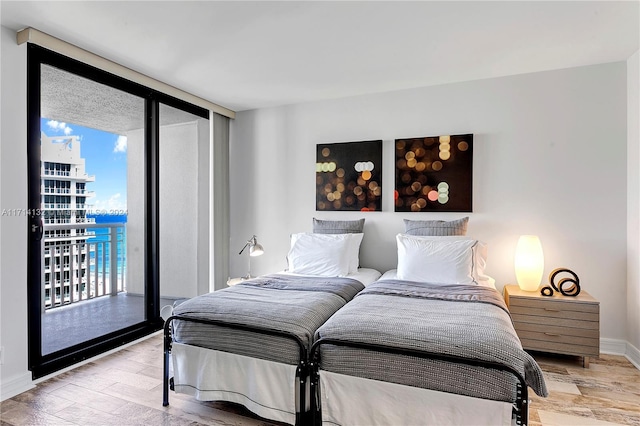 bedroom with access to outside, a wall of windows, a water view, and light wood-type flooring