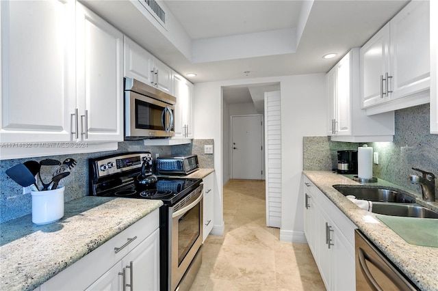 kitchen featuring decorative backsplash, light stone counters, white cabinetry, and appliances with stainless steel finishes