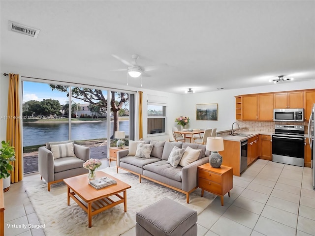 tiled living room with ceiling fan, sink, and a water view