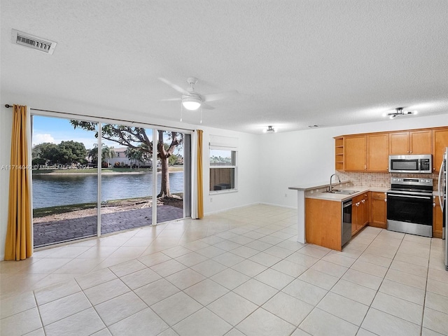 kitchen featuring stainless steel appliances, light tile patterned floors, tasteful backsplash, kitchen peninsula, and a water view