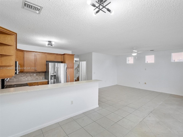 kitchen with stainless steel refrigerator with ice dispenser, ceiling fan, a textured ceiling, tasteful backsplash, and kitchen peninsula