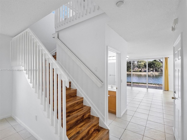 stairs with a textured ceiling, a water view, tile patterned floors, and sink