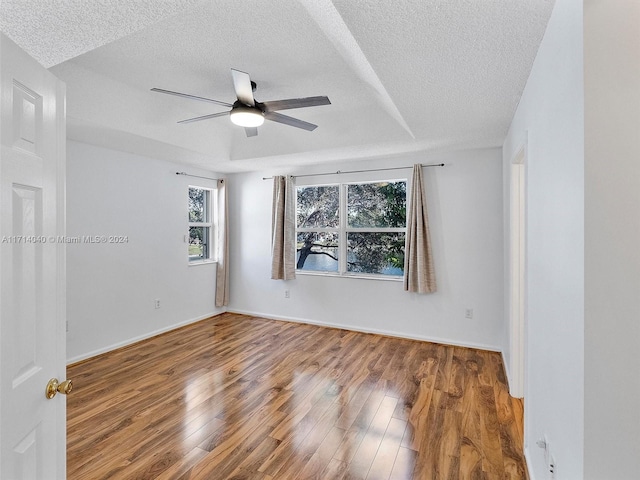 empty room featuring ceiling fan, wood-type flooring, a textured ceiling, and a tray ceiling