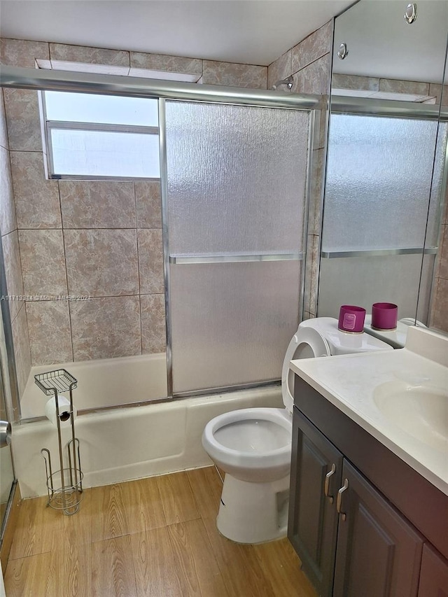 full bathroom featuring toilet, vanity, hardwood / wood-style floors, and combined bath / shower with glass door