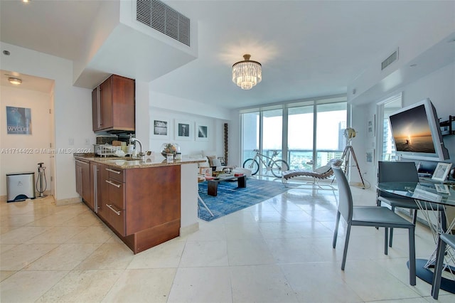 kitchen with an inviting chandelier, sink, light stone countertops, a wall of windows, and kitchen peninsula