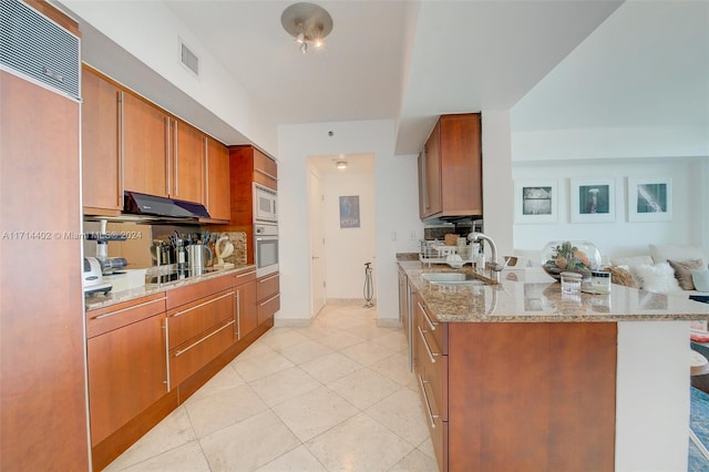 kitchen with white microwave, oven, sink, light stone countertops, and kitchen peninsula