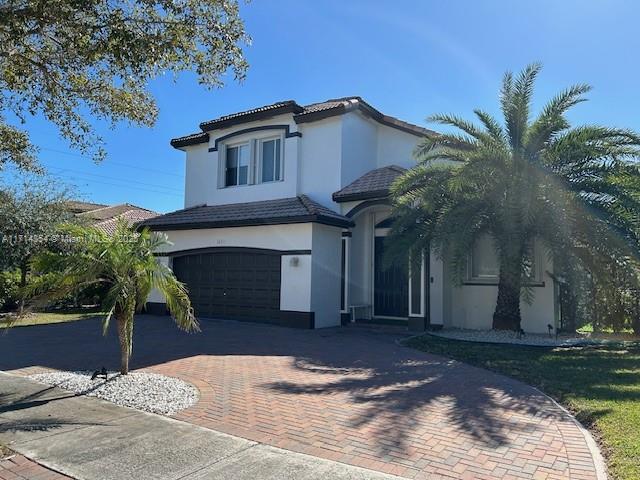 mediterranean / spanish-style house with an attached garage, a tile roof, decorative driveway, and stucco siding