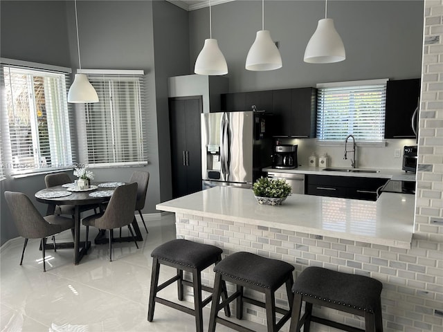 kitchen with stainless steel appliances, light countertops, hanging light fixtures, a sink, and dark cabinets