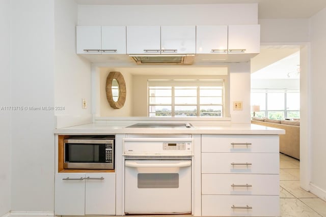 kitchen with electric cooktop, white cabinetry, light tile patterned floors, and white oven