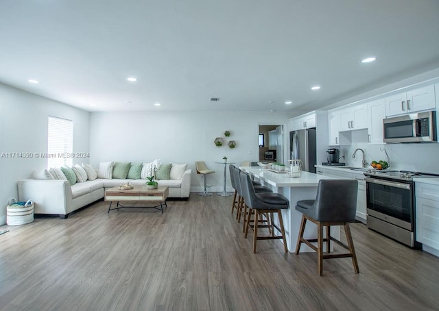 kitchen featuring hardwood / wood-style floors, a breakfast bar area, a kitchen island, white cabinetry, and stainless steel appliances