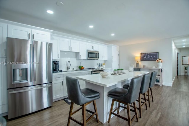 kitchen with a breakfast bar, a center island, appliances with stainless steel finishes, dark hardwood / wood-style flooring, and white cabinetry