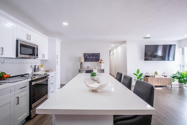 kitchen featuring appliances with stainless steel finishes, a breakfast bar, white cabinets, dark hardwood / wood-style floors, and a kitchen island