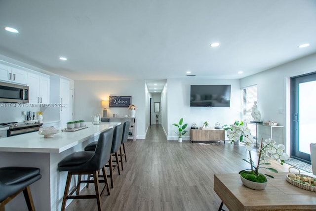 kitchen with a kitchen breakfast bar, stainless steel appliances, a center island, light hardwood / wood-style floors, and white cabinetry