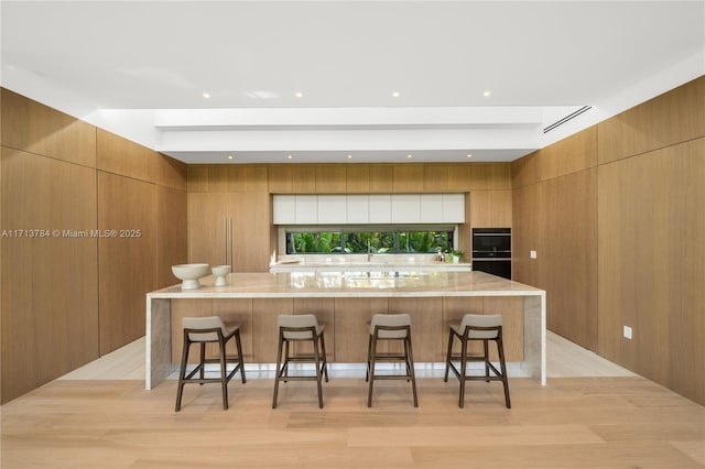 kitchen with a large island, a breakfast bar area, light stone countertops, and wood walls