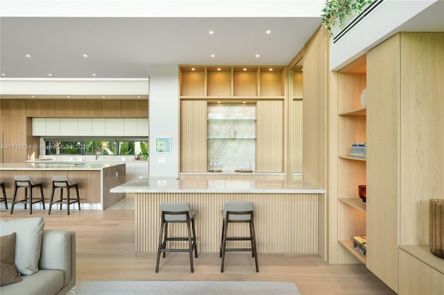 kitchen with light stone counters, a kitchen breakfast bar, built in features, and light hardwood / wood-style flooring