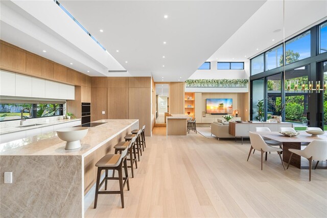 kitchen with sink, a breakfast bar, light stone counters, black electric stovetop, and light hardwood / wood-style floors