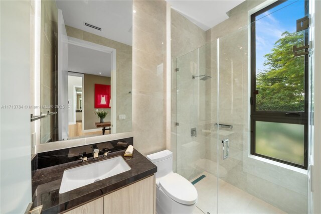 bathroom featuring vanity, a shower with shower door, tile walls, and toilet