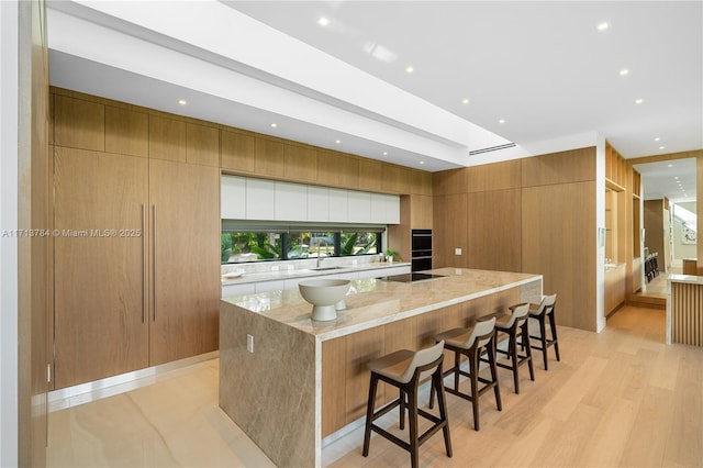 kitchen with sink, light stone counters, black electric cooktop, a kitchen breakfast bar, and a large island