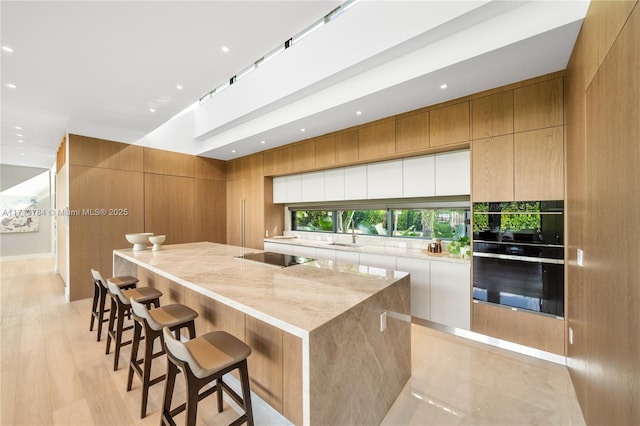 kitchen featuring sink, white cabinets, a large island, black appliances, and light stone countertops