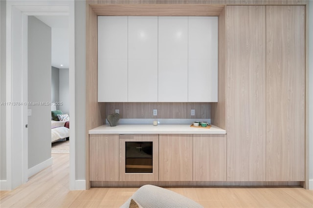 kitchen with wine cooler, light brown cabinetry, and light wood-type flooring