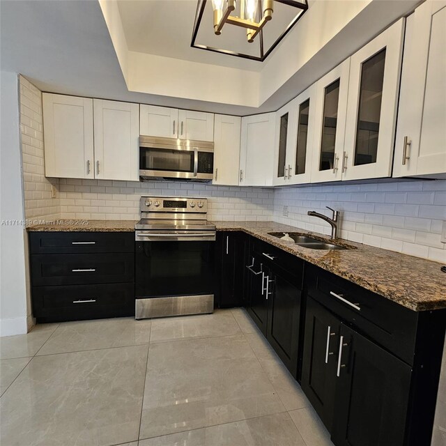 kitchen featuring stainless steel appliances, sink, white cabinetry, dark stone countertops, and backsplash