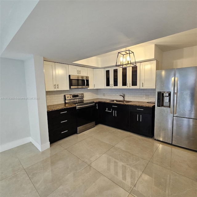 kitchen with stainless steel appliances, a sink, white cabinets, dark cabinetry, and dark stone countertops