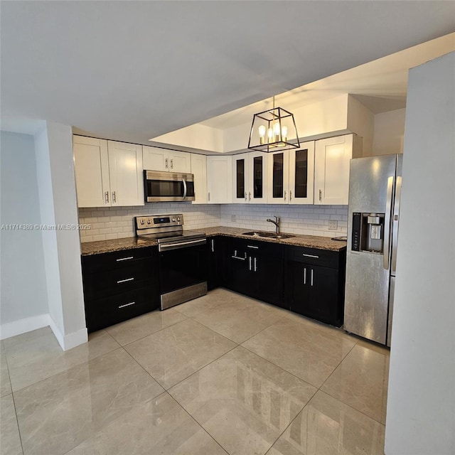 kitchen with appliances with stainless steel finishes, white cabinets, a sink, dark cabinets, and dark stone counters