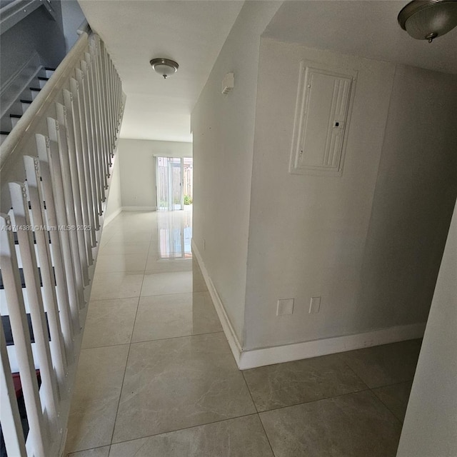 corridor with tile patterned flooring, electric panel, baseboards, and stairs