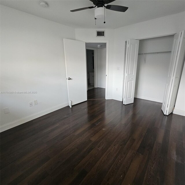 unfurnished bedroom with dark wood finished floors, a closet, visible vents, a ceiling fan, and baseboards