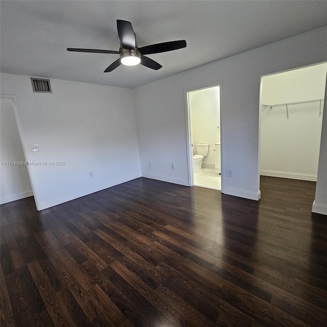 unfurnished bedroom with baseboards, visible vents, dark wood-style flooring, ensuite bathroom, and a walk in closet