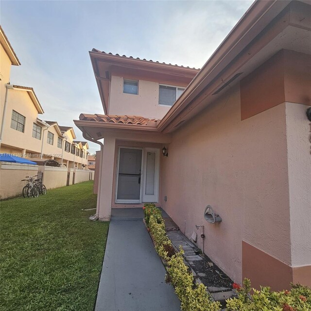 entrance to property with a tile roof, a yard, fence, and stucco siding