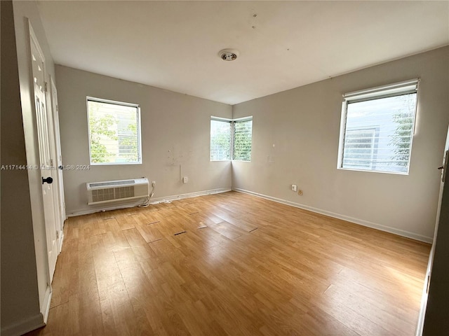 unfurnished room with a wall unit AC, light wood-type flooring, and a wealth of natural light