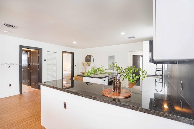 kitchen with white cabinets, light wood-type flooring, kitchen peninsula, and dark stone counters