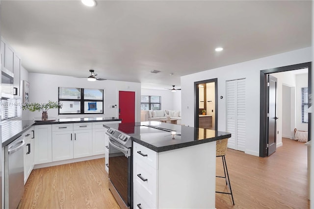 kitchen featuring a kitchen breakfast bar, stainless steel appliances, a center island, light hardwood / wood-style floors, and white cabinetry