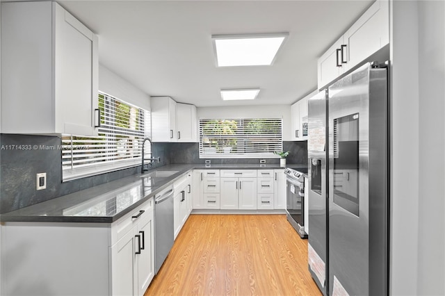 kitchen with appliances with stainless steel finishes, tasteful backsplash, sink, light hardwood / wood-style floors, and white cabinetry