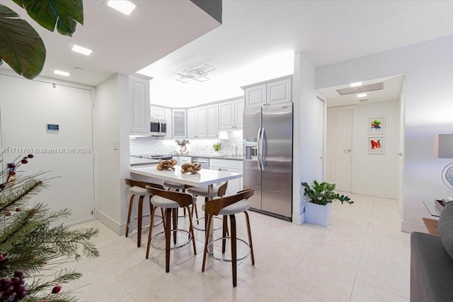 kitchen with a kitchen bar, appliances with stainless steel finishes, kitchen peninsula, backsplash, and white cabinets