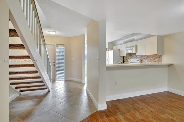 kitchen with white appliances, light wood-type flooring, kitchen peninsula, and tasteful backsplash