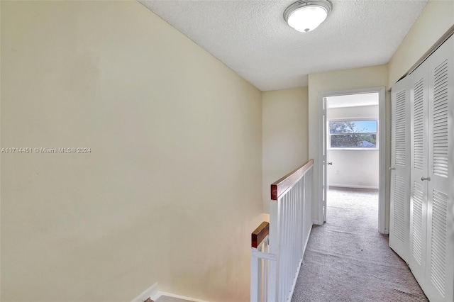 hallway with a textured ceiling and light carpet