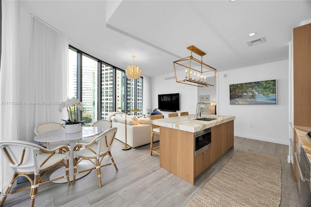 kitchen featuring sink, a center island with sink, a wall of windows, hanging light fixtures, and stainless steel microwave