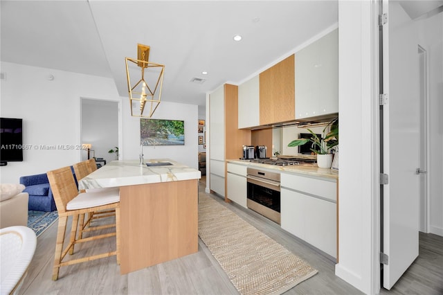 kitchen featuring white cabinets, decorative light fixtures, an island with sink, and appliances with stainless steel finishes