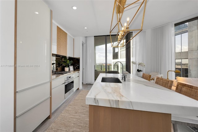 kitchen featuring sink, decorative light fixtures, white cabinetry, a wall of windows, and stainless steel appliances