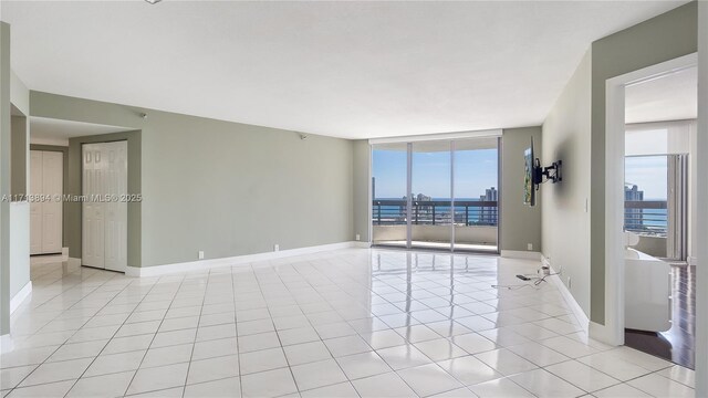 unfurnished room with light tile patterned floors, baseboards, and a wall of windows